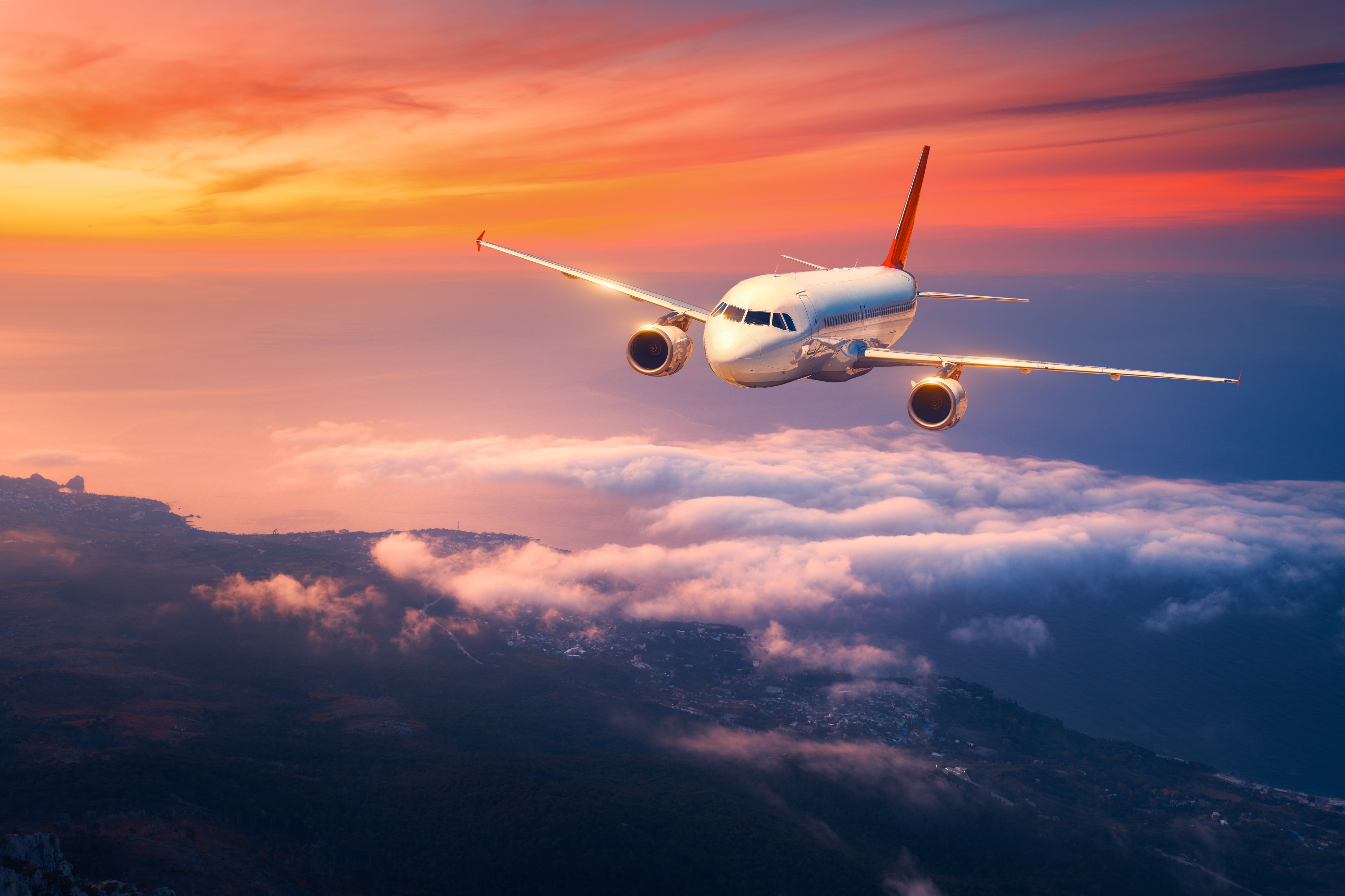 Landscape with big white airplane is flying in the sky over the clouds and sea at colorful sunset