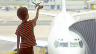 Child at the airport holding a toy plane, looking out the window towards an aerodrome